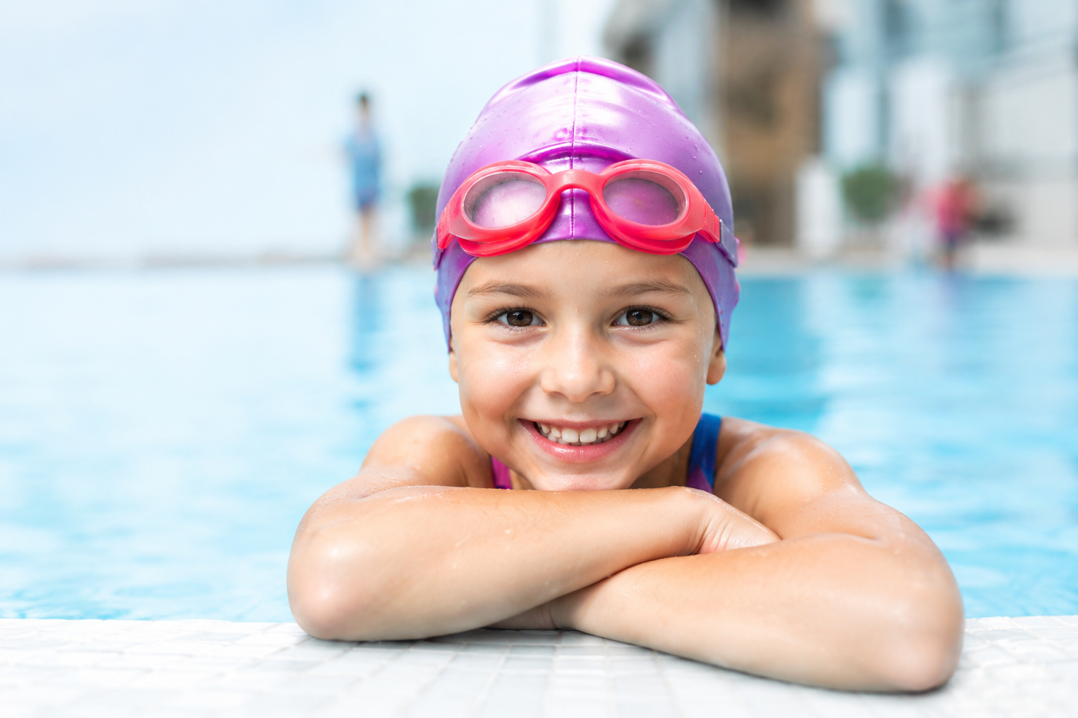 Young swimmer in a cap and goggles smiling at the poolside